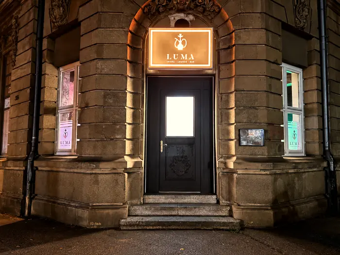Eingang der LUMA Lounge bei Nacht unter dem leuchtenden Schild